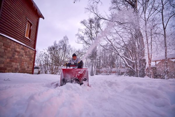 A young man clears snow with a snow blower in his back yard.